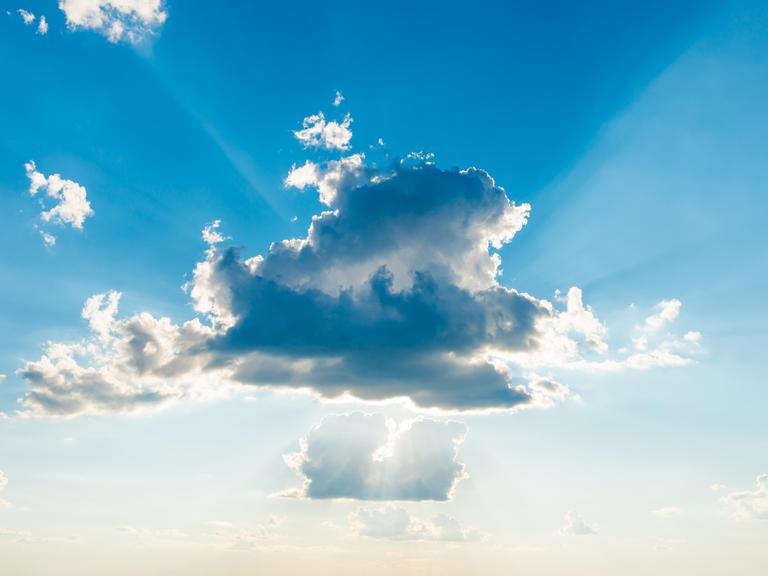 Sonnenlicht bricht durch die Wolken am blauen Himmel.