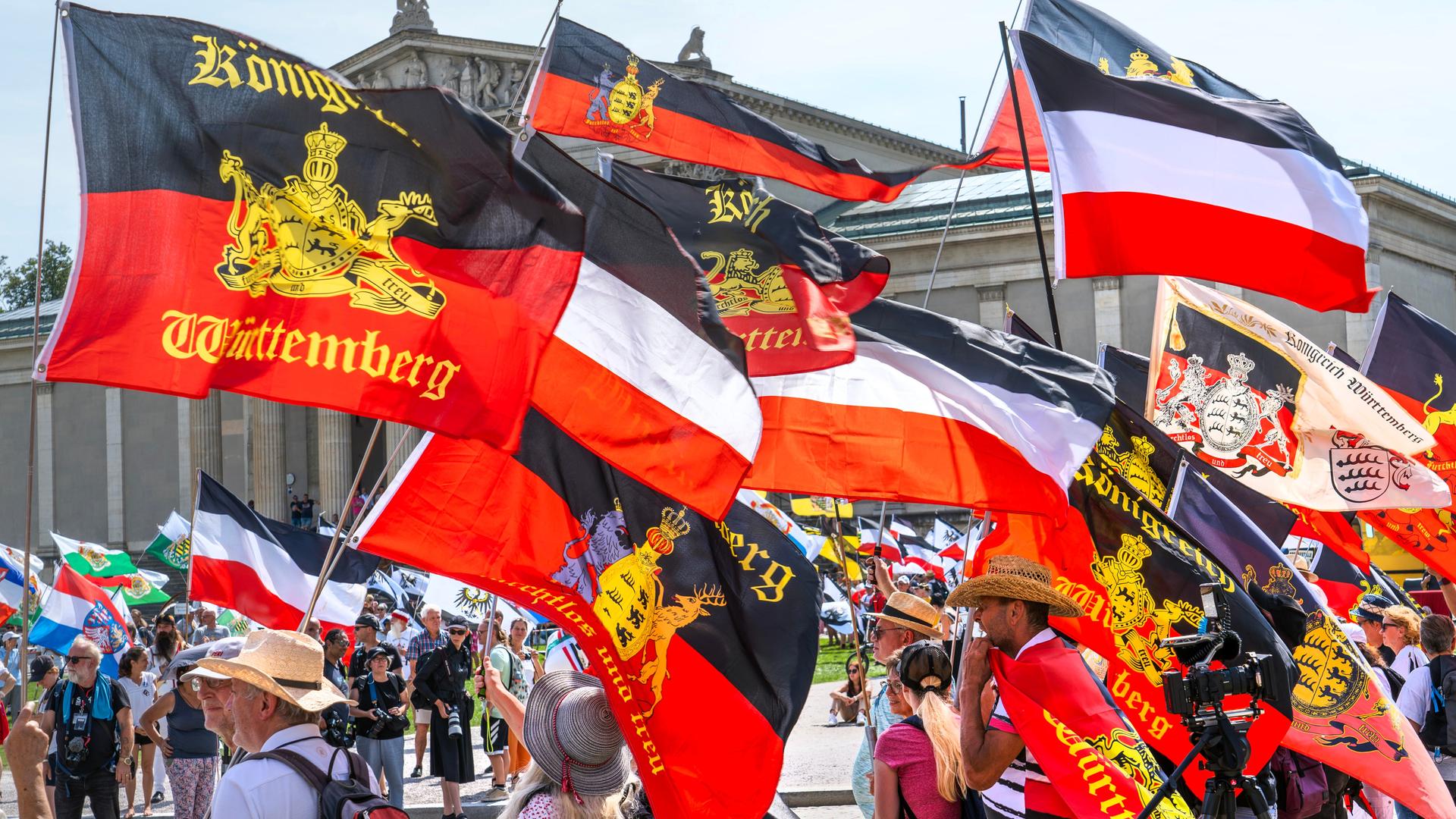 Demonstranten mit Flaggen, die im Grund alle schwarz-weiß-rot oder schwarz-rot gestreift sind und mit unterschiedlichen Symbolen belegt sind.