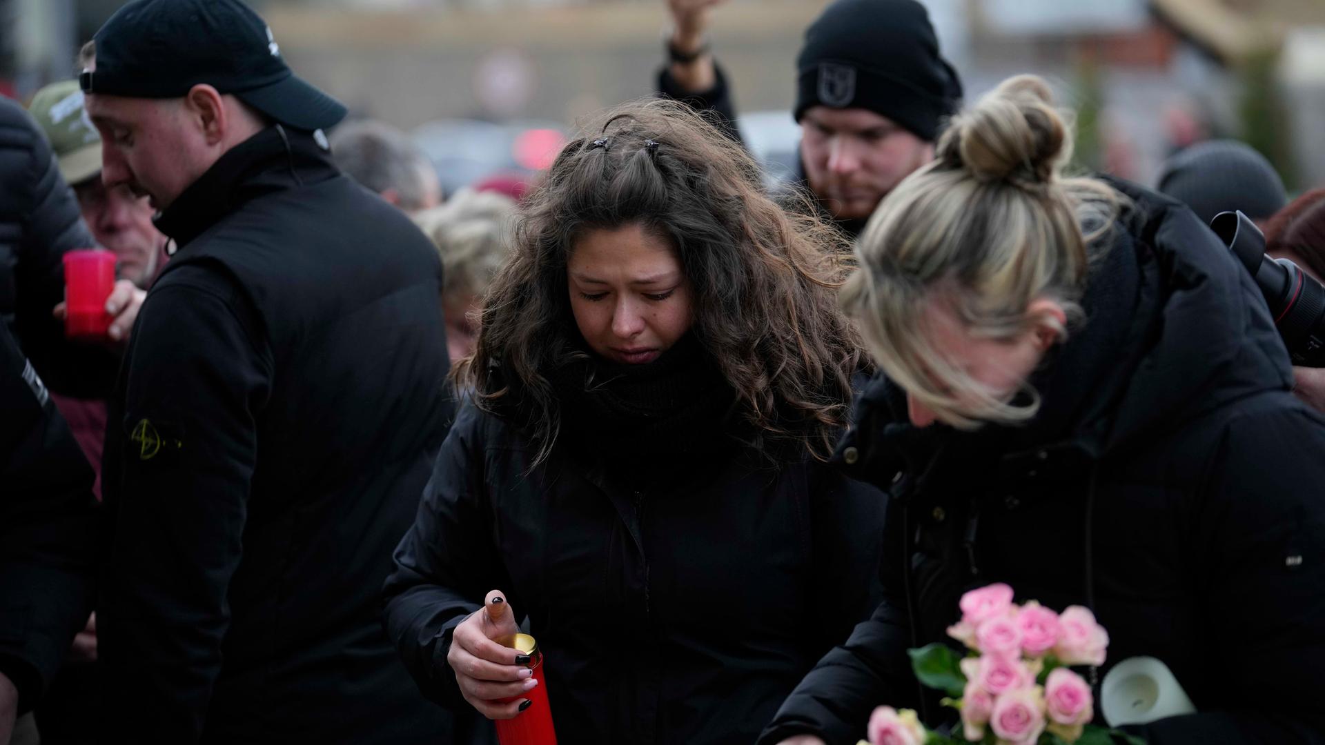 Mehrere schwarz gekleidete Menschen trauern am Magdeburger Weihnachtsmarkt. Sie legen Kerzen und Blumen ab