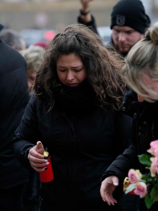 Mehrere schwarz gekleidete Menschen trauern am Magdeburger Weihnachtsmarkt. Sie legen Kerzen und Blumen ab