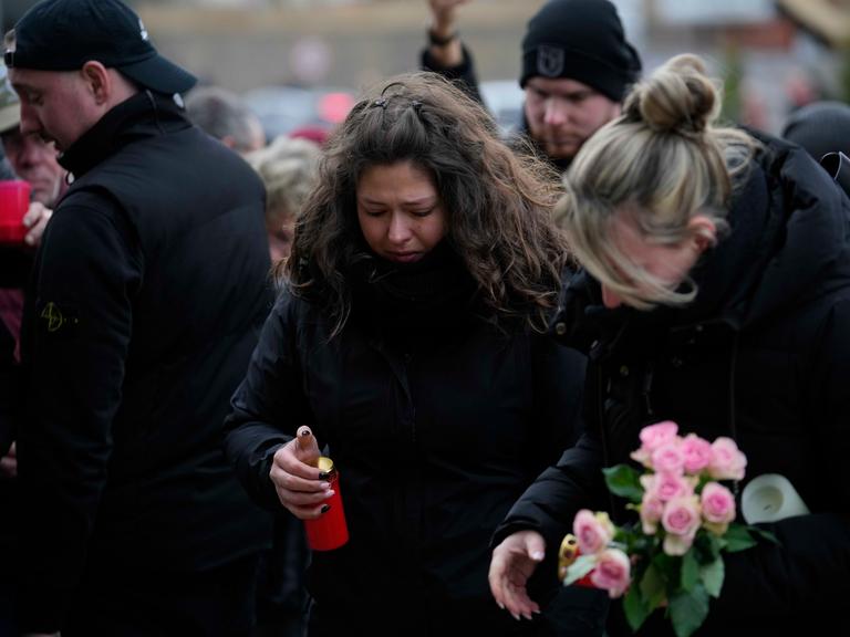 Mehrere schwarz gekleidete Menschen trauern am Magdeburger Weihnachtsmarkt. Sie legen Kerzen und Blumen ab