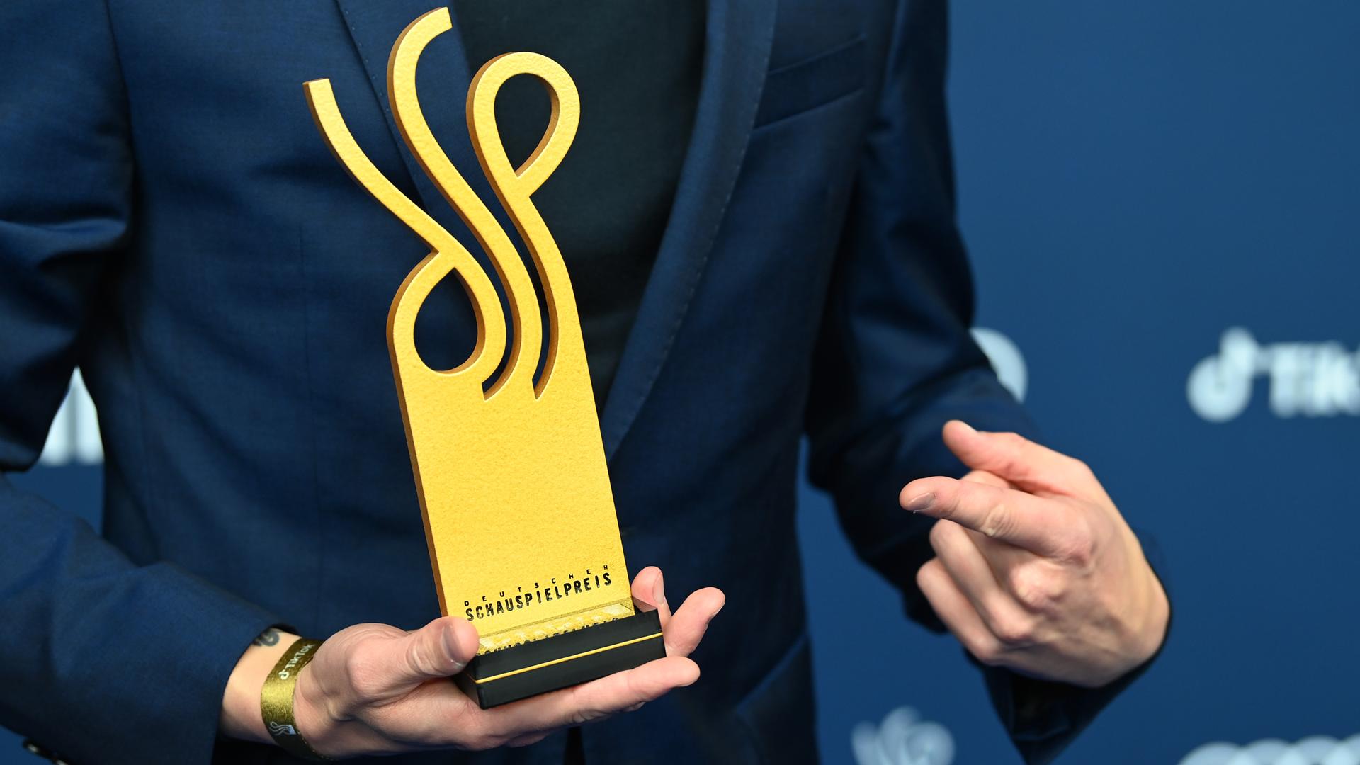 Eine Hand hält den Deutschen Schauspielpreis, die andere zeigt darauf. Eine Hand hält den Deutschen Schauspielpreis, die andere zeigt darauf.