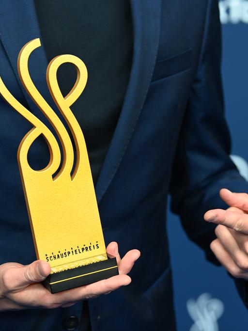 Eine Hand hält den Deutschen Schauspielpreis, die andere zeigt darauf.