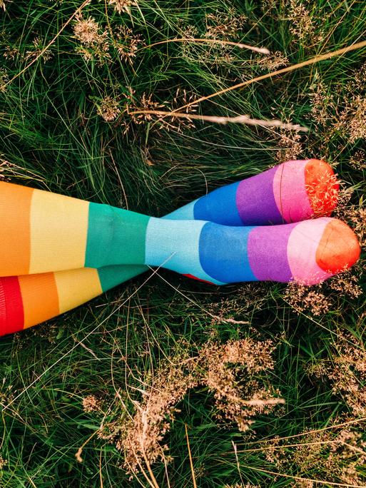 Eine Frau liegt auf einer Wiese und trägt regenbogenfarbene Socken.