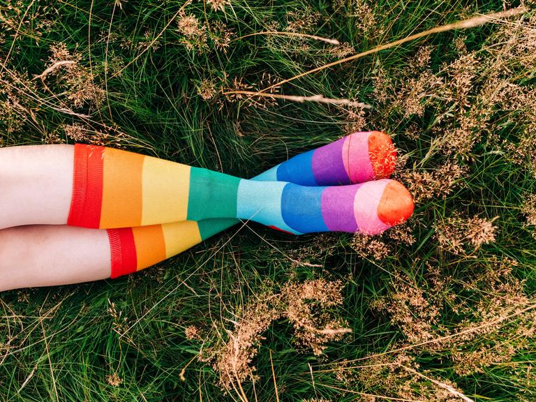 Eine Frau liegt auf einer Wiese und trägt regenbogenfarbene Socken.