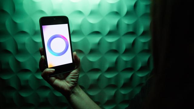 Eine Hand hält ein Smartphone, auf dem das Meta-Logo für ihre KI angezeigt wird: Ein Ring aus ineinanderfließenden Farben in Blau, Lila und Pink.