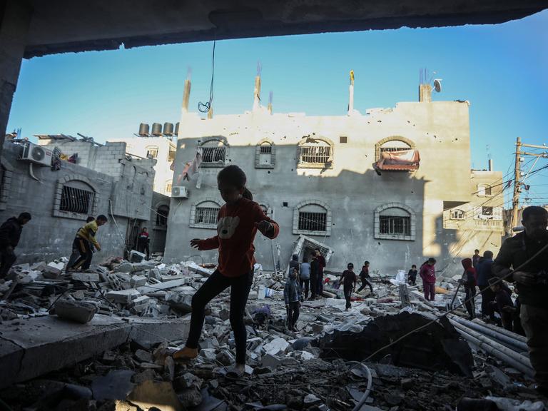 Menschen laufen über Trümmer von Häusern in Rafah im Gazastreifen