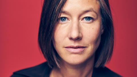 Portrait einer Frau mit halblangem Haar vor rotem Hintergrund