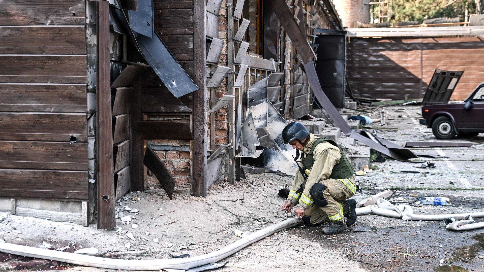 Ein Feuerwehrmann kniet mit einem Wasserschlauch vor einer zerstörten Hütte.