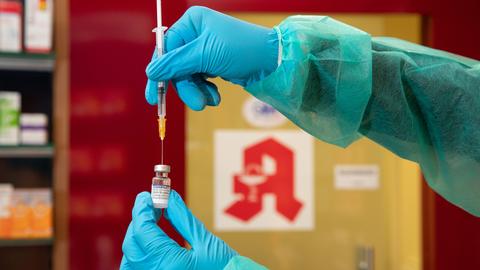 Eine Apothekerin zieht während einer gestellten Situation in ihrer Apotheke einen Impfstoff mit einer Spritze auf.