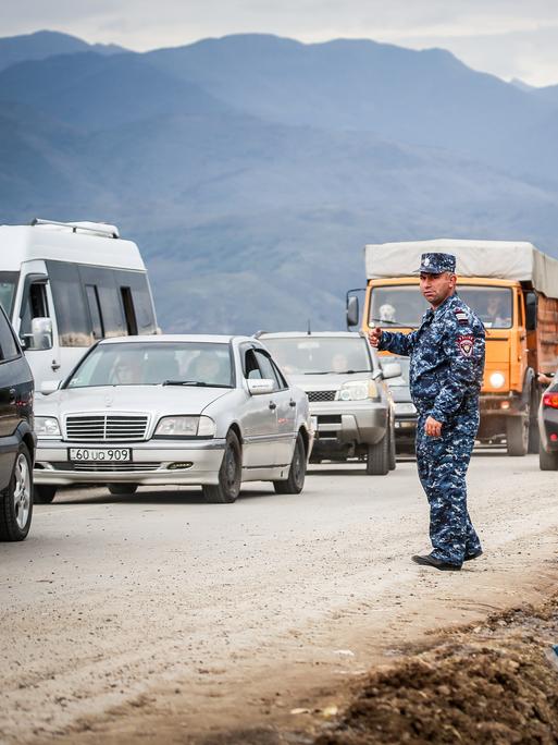 Viele Autos fahren auf einer Straße im Grenzgebiet zwiswchen Armenien und Aserbaidschan, imi Vordergrund steht ein Polizist.