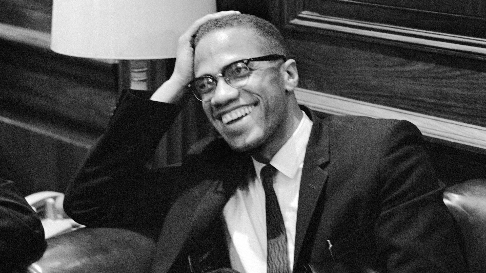 Der US-Bürgerrechtler Malcolm X im Anzug, er sitzt lächelnd auf einem Sessel und wartet auf die Pressekonferenz von Martin Luther King im Jahr 1964. Der US-Bürgerrechtler Malcolm X im Anzug, er sitzt lächelnd auf einem Sessel und wartet auf die Pressekonferenz von Martin Luther King im Jahr 1964.