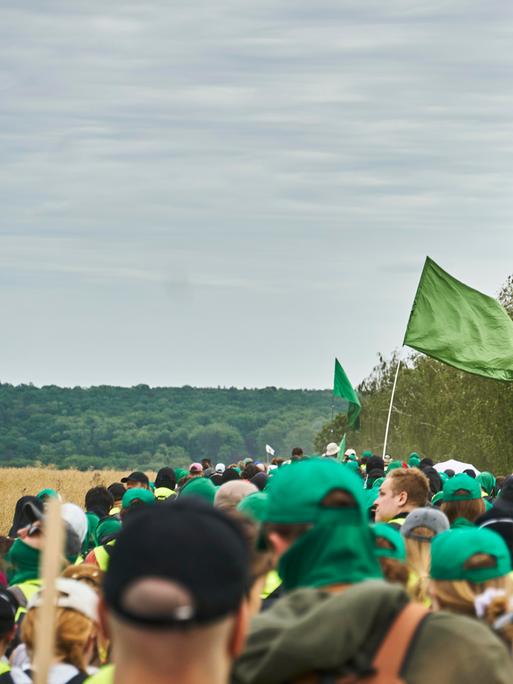 Eine große Gruppe von Menschen läuft gemeinsam über Land. Die meisten tragen grüne Basecaps. Eine grüne Fahne wird geschwenkt, außerdem die Flagge der "Antifaschistischen Aktion". Eine große Gruppe von Menschen läuft gemeinsam über Land. Die meisten tragen grüne Basecaps. Eine grüne Fahne wird geschwenkt, außerdem die Flagge der "Antifaschistischen Aktion".