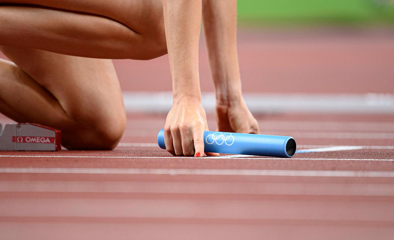 Eine Leichtathletin hält beim 4x400 Meter Staffellauf den Staffelstab beim Start in der rechten Hand.