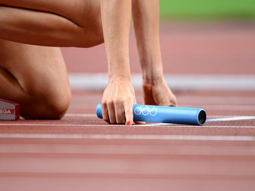 Eine Leichtathletin hält beim 4x400 Meter Staffellauf den Staffelstab beim Start in der rechten Hand.