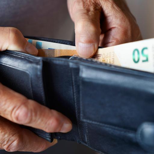 Eine alte Hand hält ein Portemonnaie und zieht einen 50-Euro-Schein heraus.
