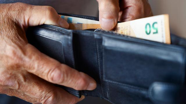 Eine alte Hand hält ein Portemonnaie und zieht einen 50-Euro-Schein heraus.