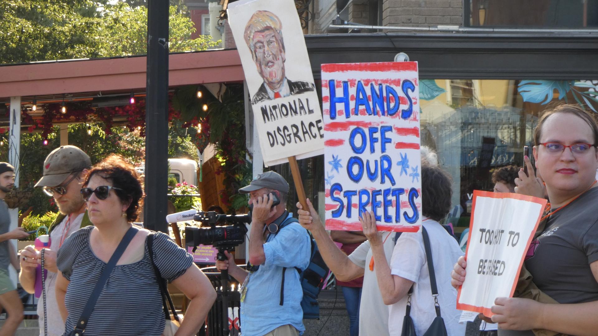 Mehrere Menschen mit Transparenten stehen vor einem Gebäude. Auf einem Schild steht "Hands off our Streets". 