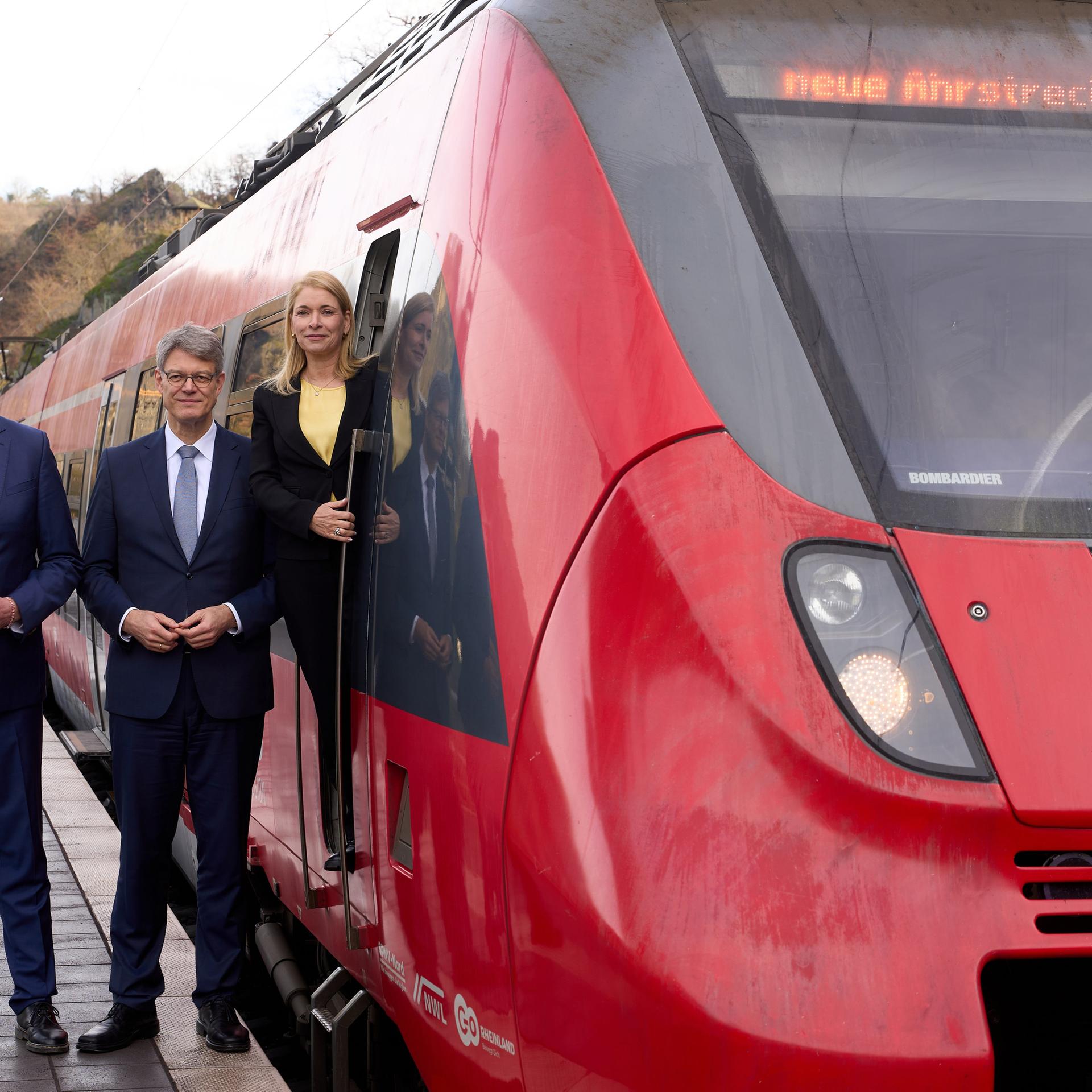 Der rheinland-pfälzische Ministerpräsident Alexander Schweitzer, Bundesverkehrsminister Patrick Schnieder und Bahnchefin Evelyn Palla stehen neben der geöffneten Tür einer Lok der Ahrtalbahn und schauen in die Kamera. Der Zug ist rot.