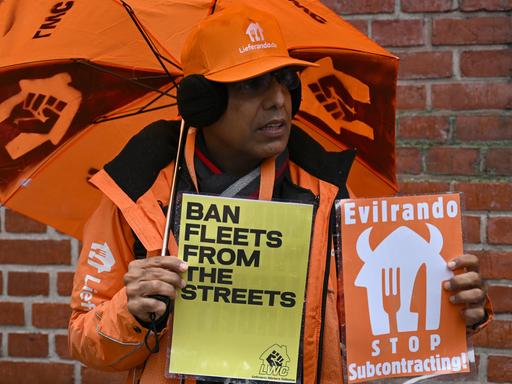 Ein Teilnehmer eines Streiks bei Lieferando hält zwei Protestschilder hoch. Die Gewerkschaft Nahrung-Genuss-Gaststätten (NGG) hat die insgesamt etwa 1.900 Essenskuriere und Support-Mitarbeiter aufgerufen, die Arbeit niederzulegen.