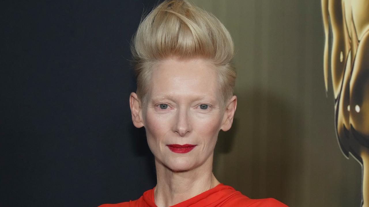 Tilda Swinton bei einem Event in Los Angeles. Die weiß-blonden Haare sind hoch toupiert, sie trägt ein rotes Oberteil. 