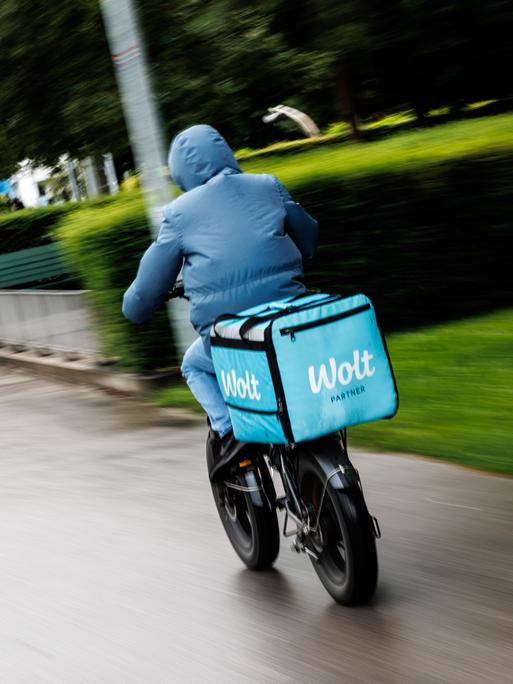 Ein Wolt-Fahrradkurier fährt durch einen Park