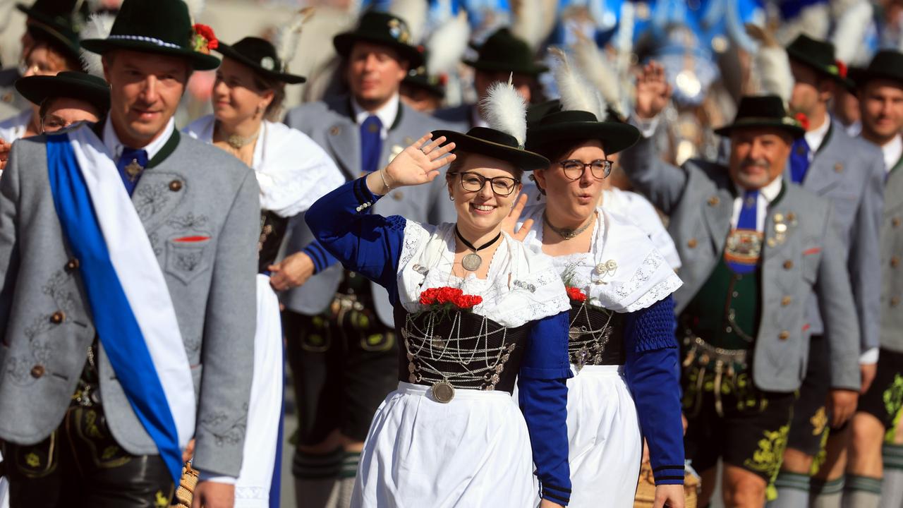 Teilnehmerinnen und Teilnehmer des Trachtenumzugs ziehen durch die Innenstadt. Eine Frau winkt in die Kamera.