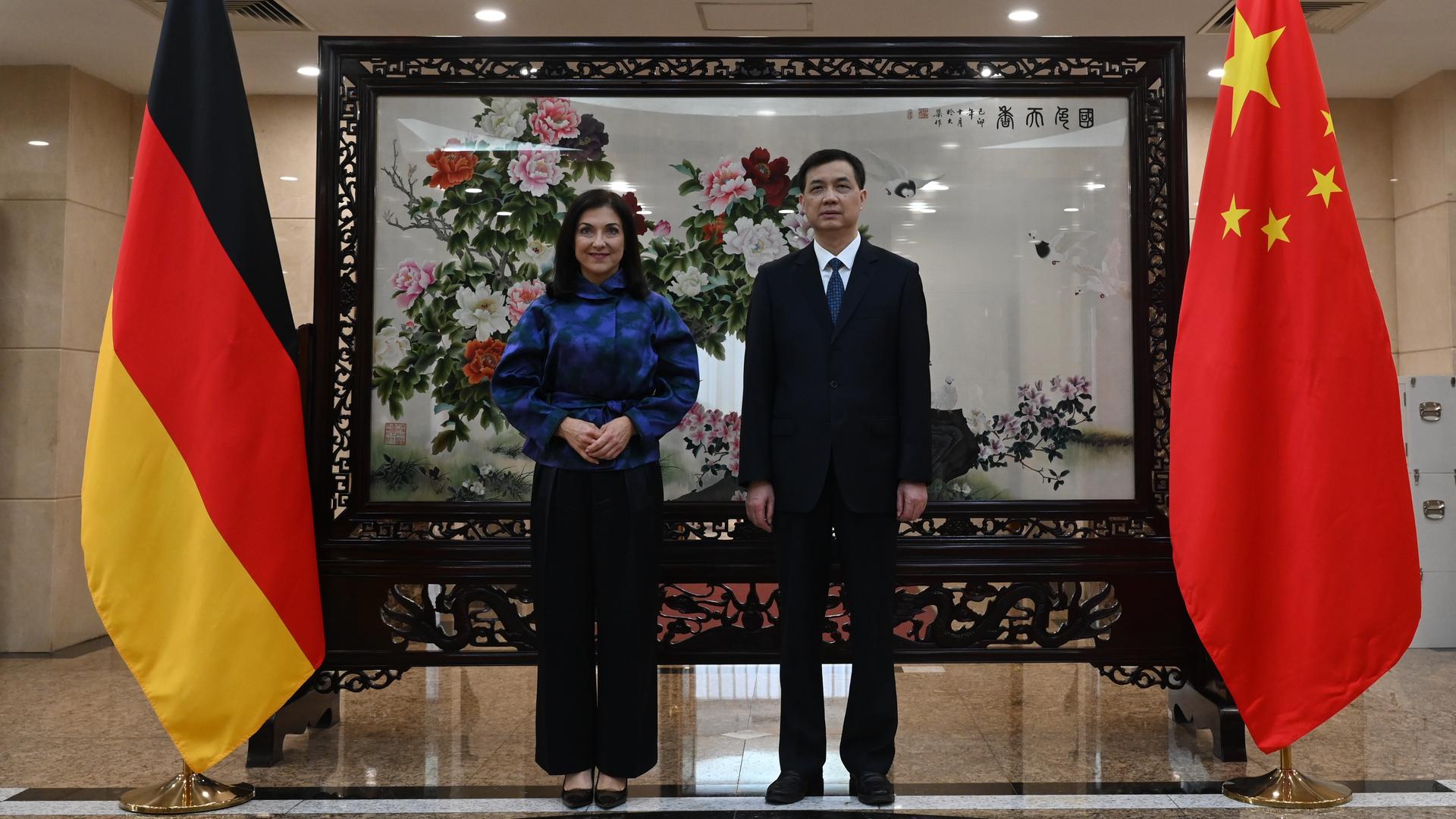 Das Bild zeigt Katherina Reiche und ihren chinesischen Gastgeber Zhou Haibing. Sie stehen nebeneinander und schauen in Richtung der Kameras. Neben ihnen sind die Flaggen Deutschlands und Chinas zu sehen.