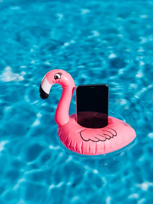 Ein Smartphone auf einem Gummi-Flamingo in einem Pool.