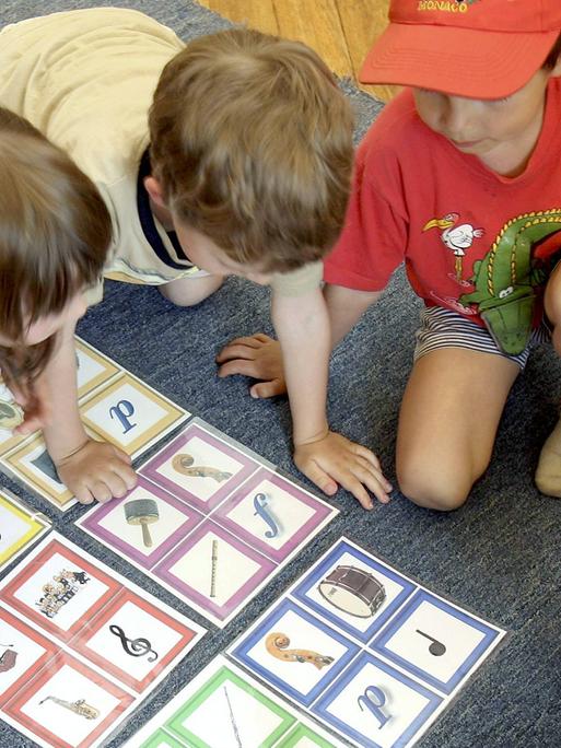 Eine Schar junger Kinder kniet um ein Memory, das musikalische Symbole wie den Notenschlüssel oder eine Pauke zeigt. 