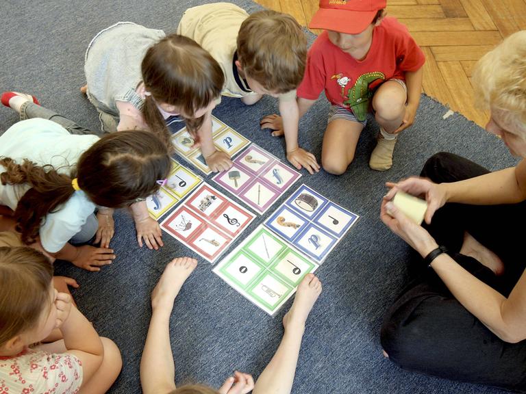 Eine Schar junger Kinder kniet um ein Memory, das musikalische Symbole wie den Notenschlüssel oder eine Pauke zeigt. 