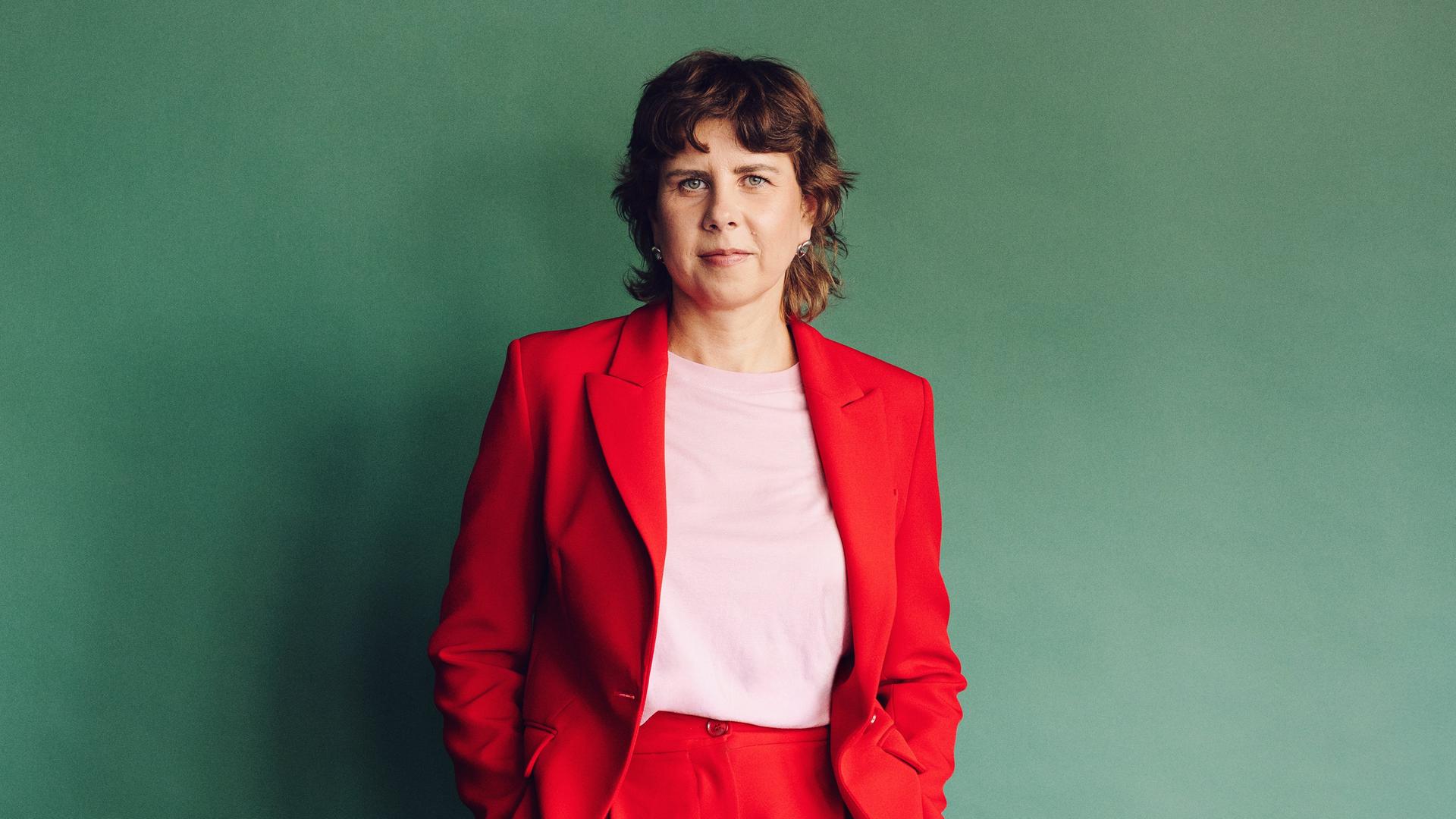 Gitte Zschoch trägt einen knallroten Zweiteiler und steht vor einer dunkelgrünen Wand.