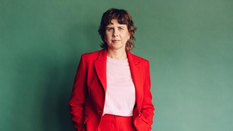Gitte Zschoch trägt einen knallroten Zweiteiler und steht vor einer dunkelgrünen Wand.