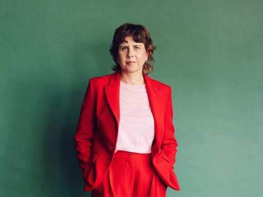 Gitte Zschoch trägt einen knallroten Zweiteiler und steht vor einer dunkelgrünen Wand.