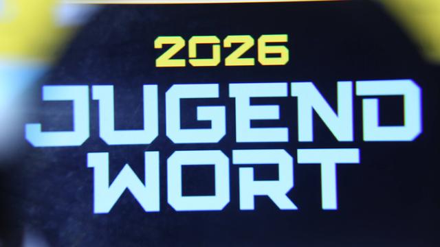 Auf einem Bild-Schirm steht die Jahres-Zahl 2026. Darunter steht Jugend-Wort des Jahres.