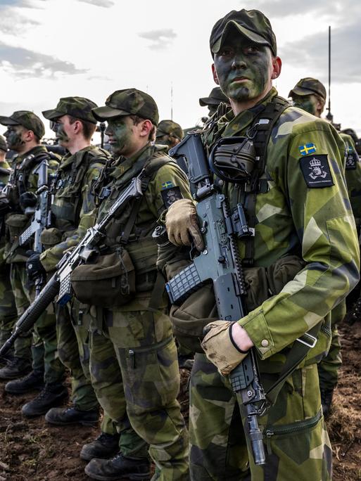 Schwedische Soldaten stehen mit Gewehren vor einer Reihe von Panzern