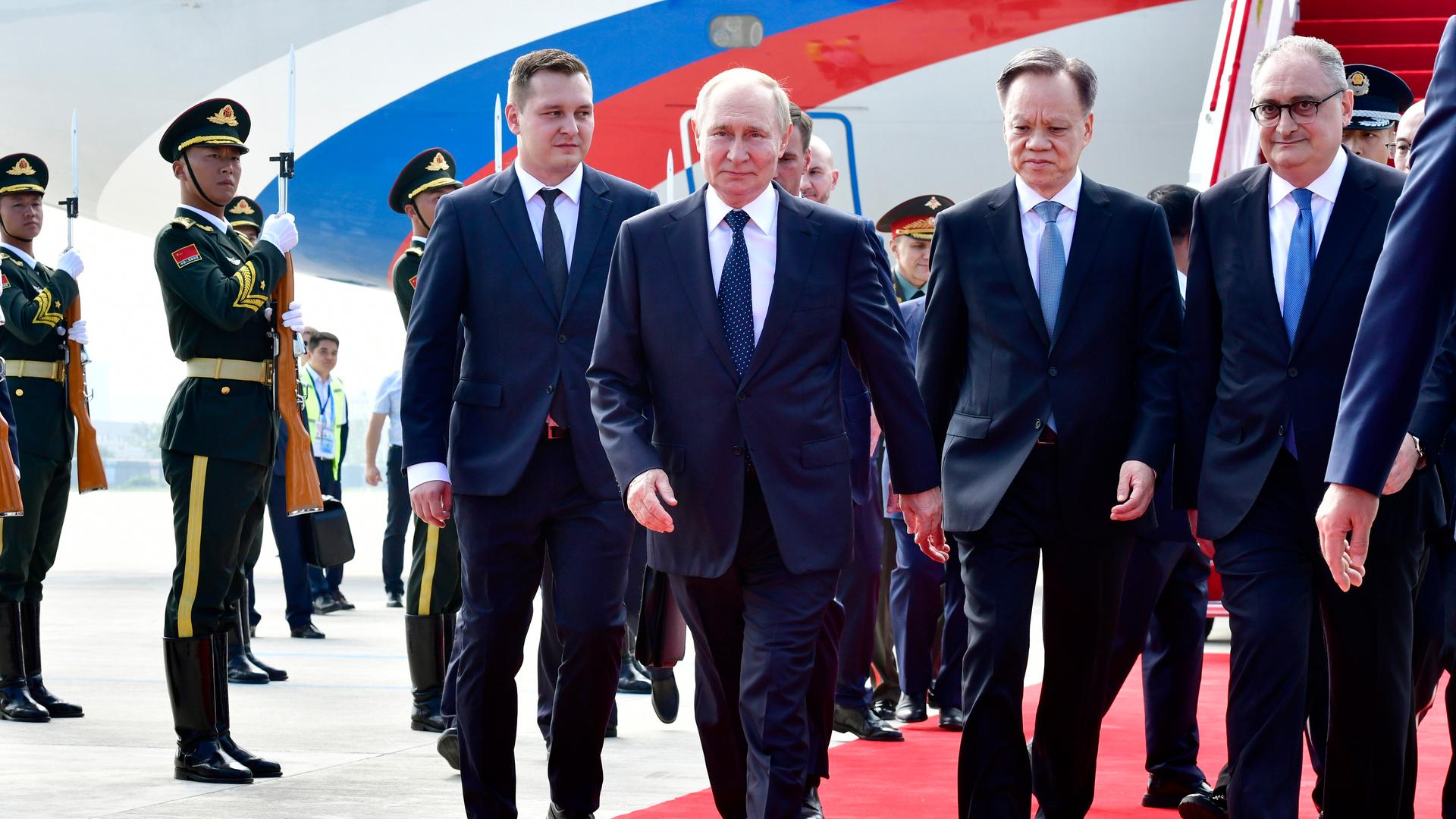 Russands Präsident Putin schreitet über einen roten Teppich. Links und rechts neben ihm stehen weitere Männer in Anzügen. Im Hintergrund sieht man Soldaten, die salutieren. Russands Präsident Putin schreitet über einen roten Teppich. Links und rechts neben ihm stehen weitere Männer in Anzügen. Im Hintergrund sieht man Soldaten, die salutieren.