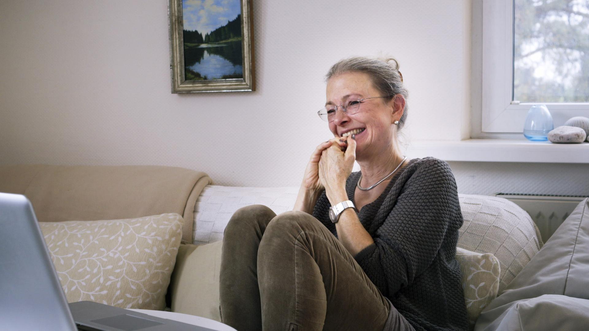 Filmstill aus der Doku: "ER SIE ICH" von Carlotta Kittel. Die Mutter sitzt auf einem Sofa und lacht.