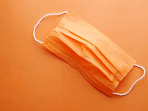Eine orangene Corona-Maske vor orangenem Hintergrund.