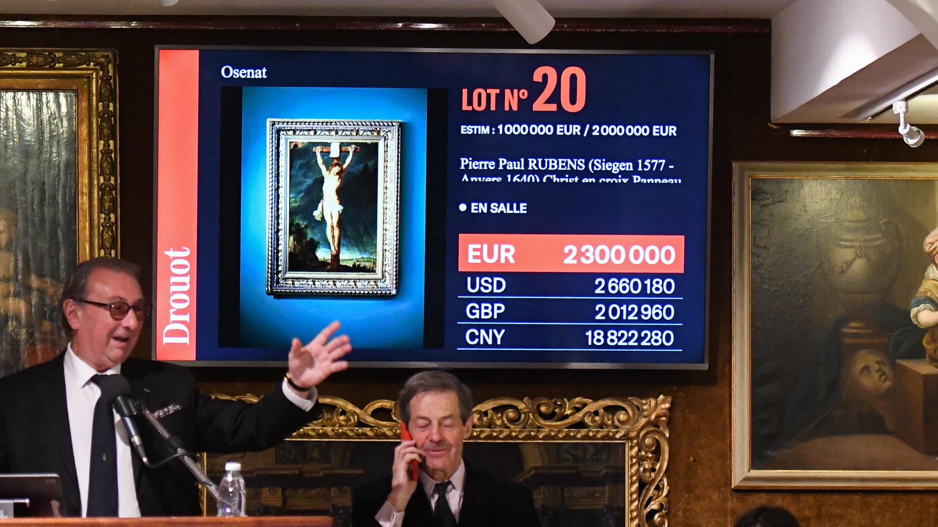 Das Gemälde „Christus am Kreuz“ des flämischen Meisters Peter Paul Rubens ist auf einem Monitor hinter dem gestikulierenden Auktionator zu sehen.


