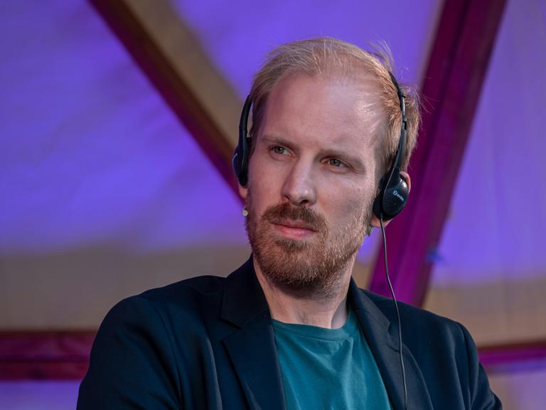 Der niederländische Historiker und Autor Rutger Bregman hört mit einem Headset aufmerksam der Übersetzung einer Rede in Barcelona zu.