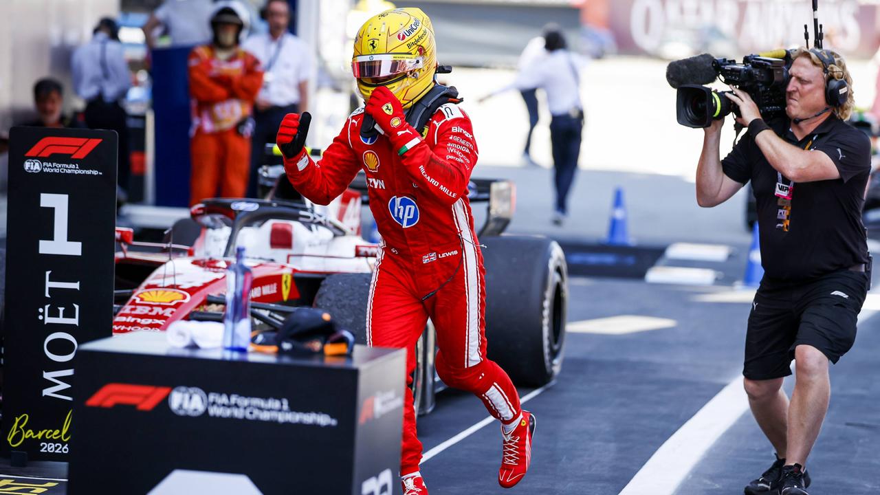 Lewis Hamilton macht eine Siegerpose neben seinem Ferrari. Er trägt einen gelben Helm und einen roten Rennanzug. 