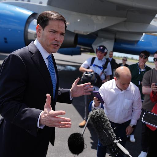 US-Außenminister Rubio steht vor Pressevertretern und spricht in Mikrofone. Er ist auf einem Flughafen. Im Hintergrund ist ein Flugzeug zu sehen. 