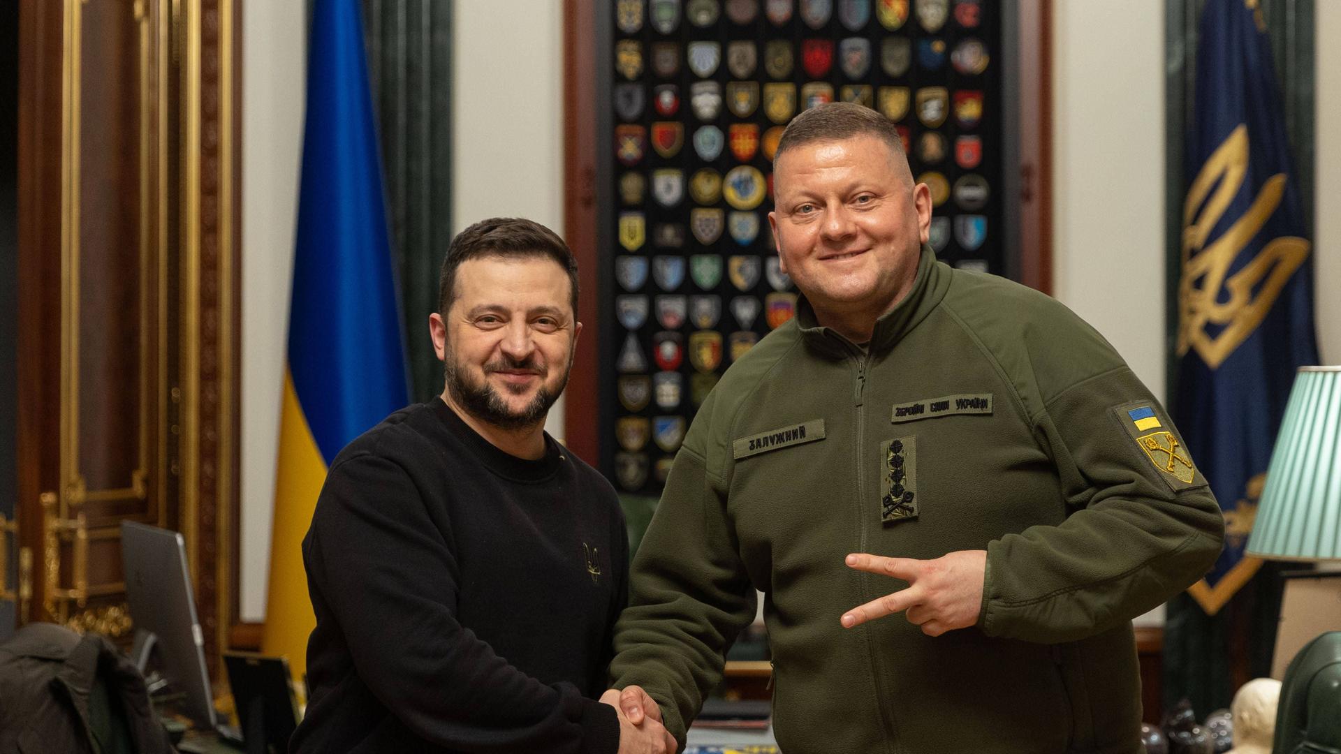 Man sieht den ukrainischen Präsident Wolodymyr Selenskyj mit dem ehemaligen Oberkommandierenden der ukrainischen Streitkräfte, Walerij Saluschnyj. Sie geben sich die Hand.