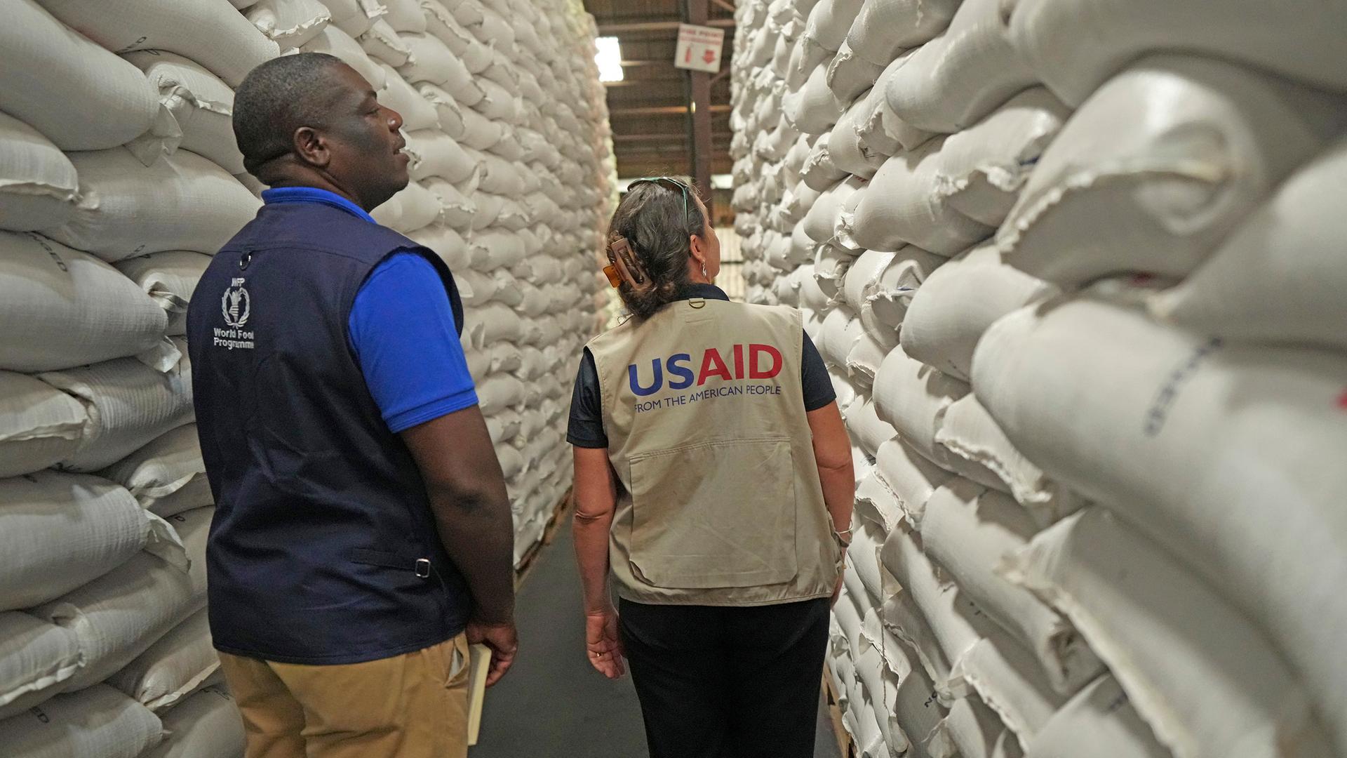 Ein Mitarbeiter des Welternährungsprogramms und eine Mitarbeiterin von USAID inspizieren Getreidesäcke in einer Lagerhalle.