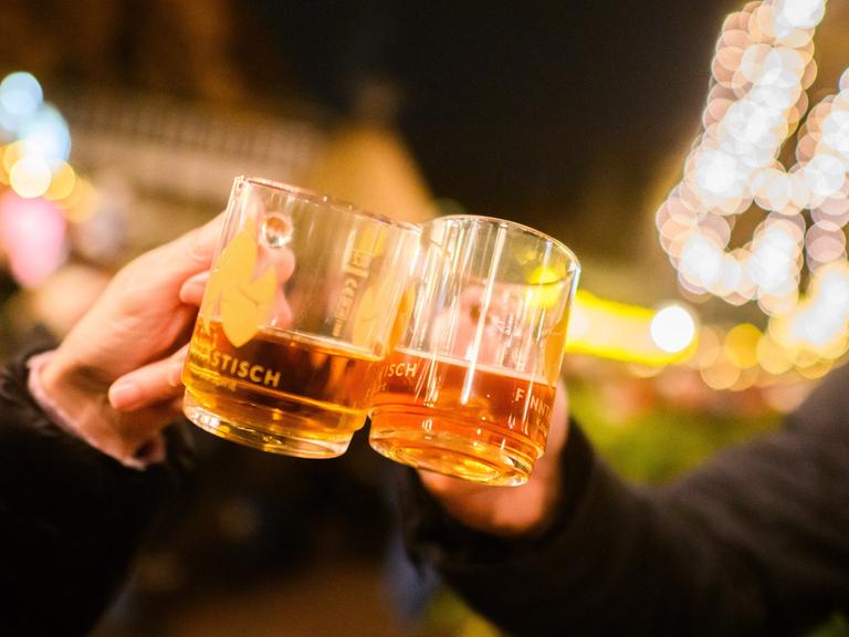 Besucher stoßen mit weißem Glühwein auf dem Weihnachtsmarkt an.