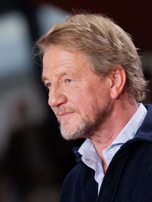 Der Regisseur Sönke Wortmann kommt über den Roten Teppich zur Premiere des Kinofilms "Eingeschlossene Gesellschaft". Er trägt einen blauen Pullover und darunter ein Hemd.
