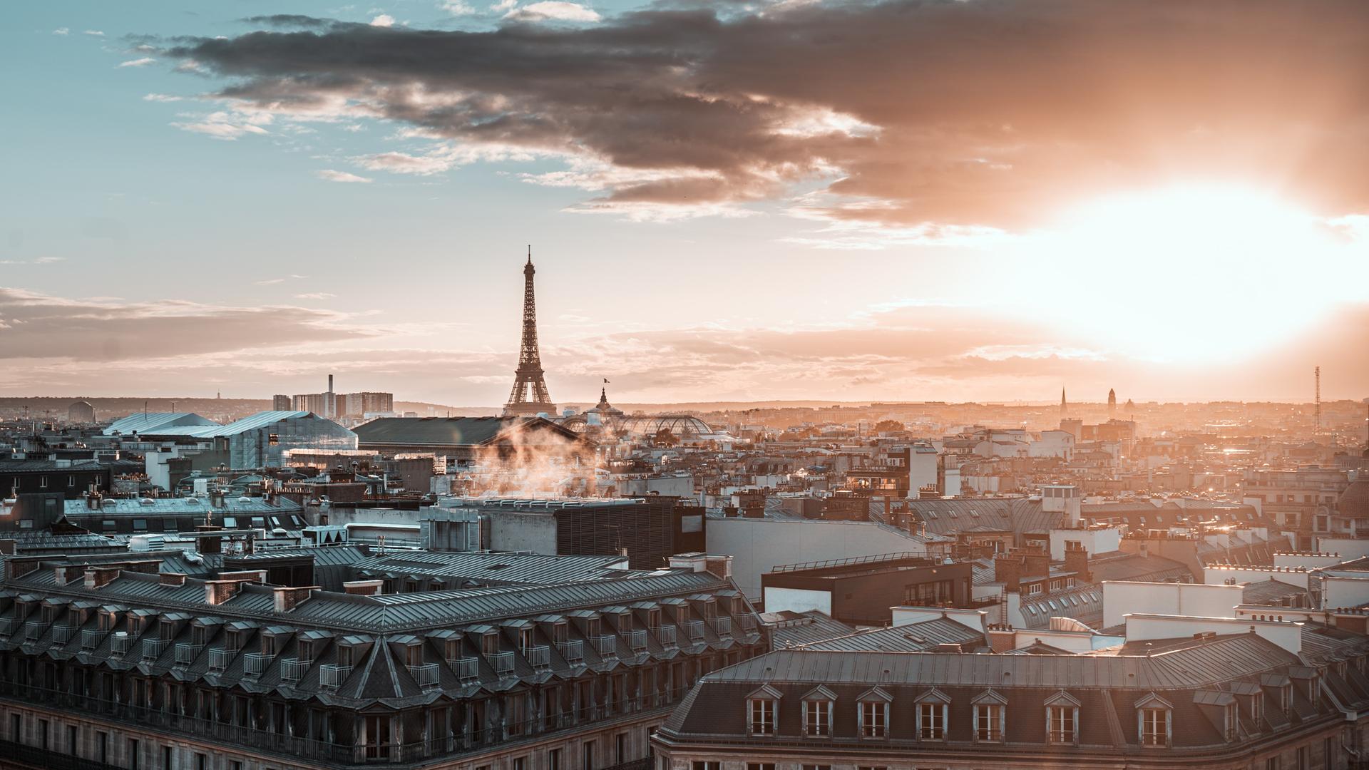 Blick über die Stadt Paris mit Eifelturm und großen Wolken bei einem diesigen Sonnenuntergang.