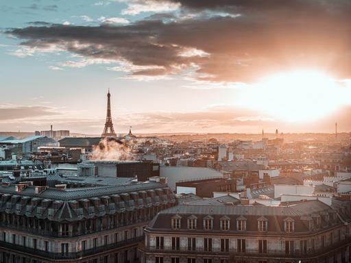 Blick über die Stadt Paris mit Eifelturm und großen Wolken bei einem diesigen Sonnenuntergang.
