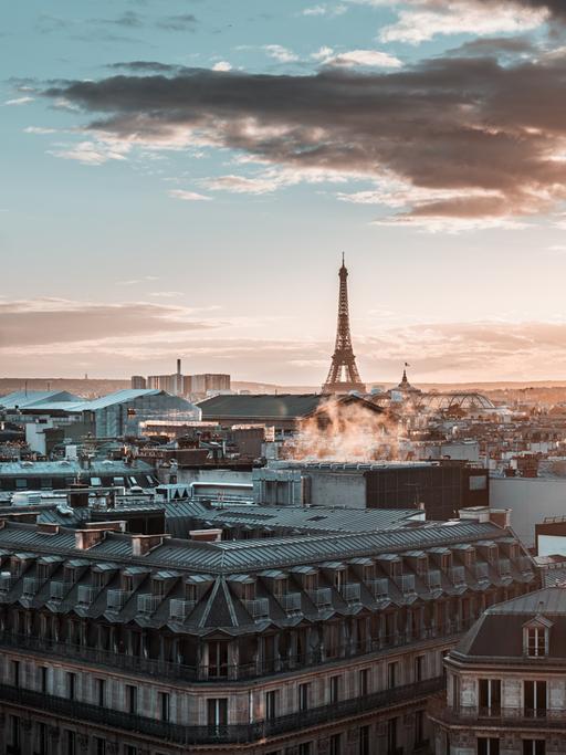 Blick über die Stadt Paris mit Eifelturm und großen Wolken bei einem diesigen Sonnenuntergang.